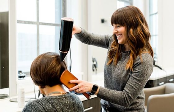 A hair dresser blow drying a customers hair and combing it