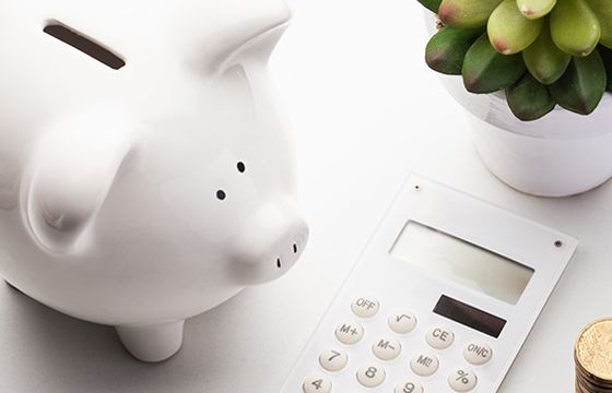 A white piggy bank resting next to a calculator