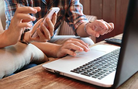 Two people sitting side by side researching fraud protection on a laptop and phone