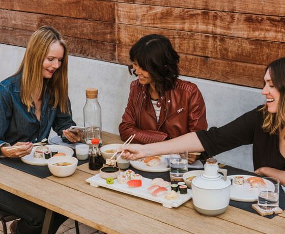Three female friends enjoying sushi with each other while using Zelle to send money to one another through the Stellar Bank App