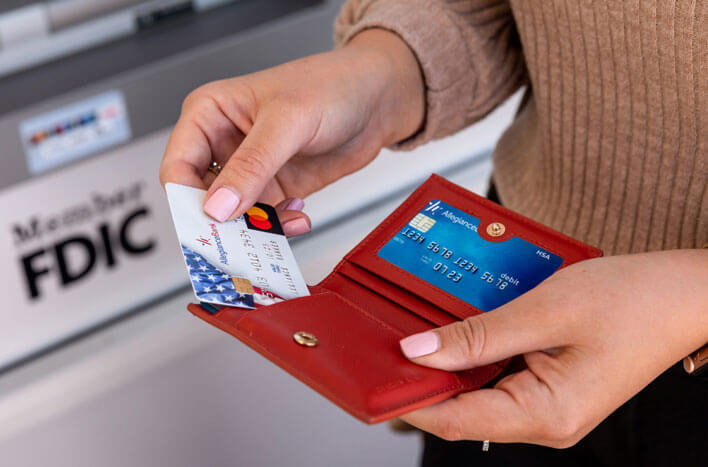 Someone pulling their credit card out of their wallet at an ATM