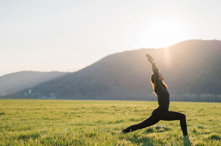 A person doing yoga in a grassy field with the sun behind them