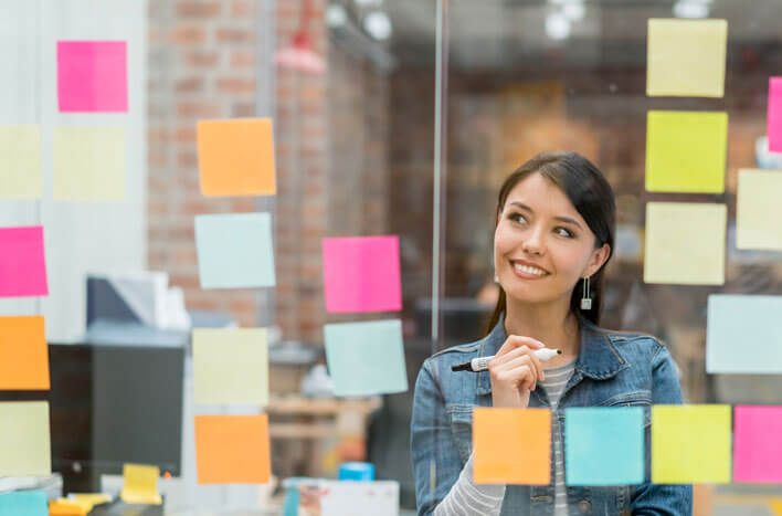 A woman posting sticky notes on a glass window while thinking of ideas