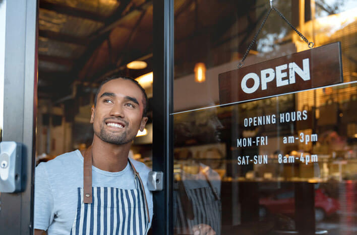 A male barista looking outside the door of a coffee shop